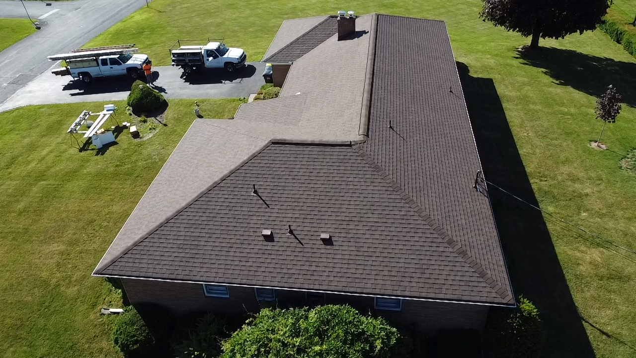 Aerial Side View of Brown Shingle Roof on a Brick Ranch Home with New Roof and Roofer Trucks